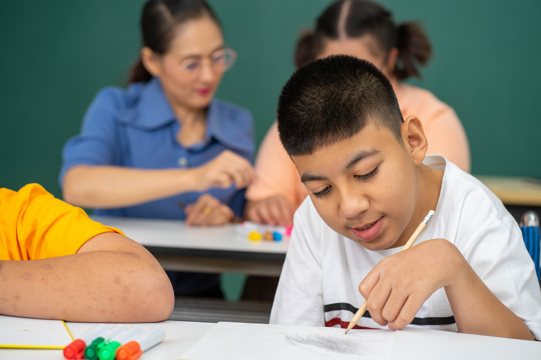 Boy with Disability in Classroom Studying with Asian Teacher