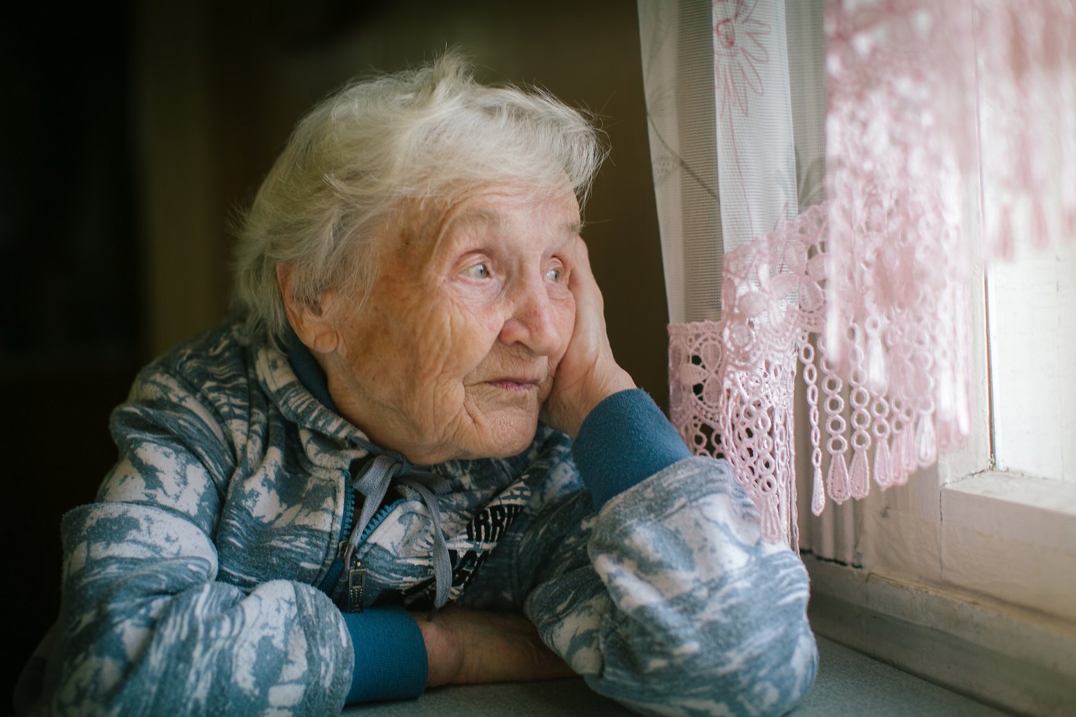 Elderly woman sitting at the table looking out the window.